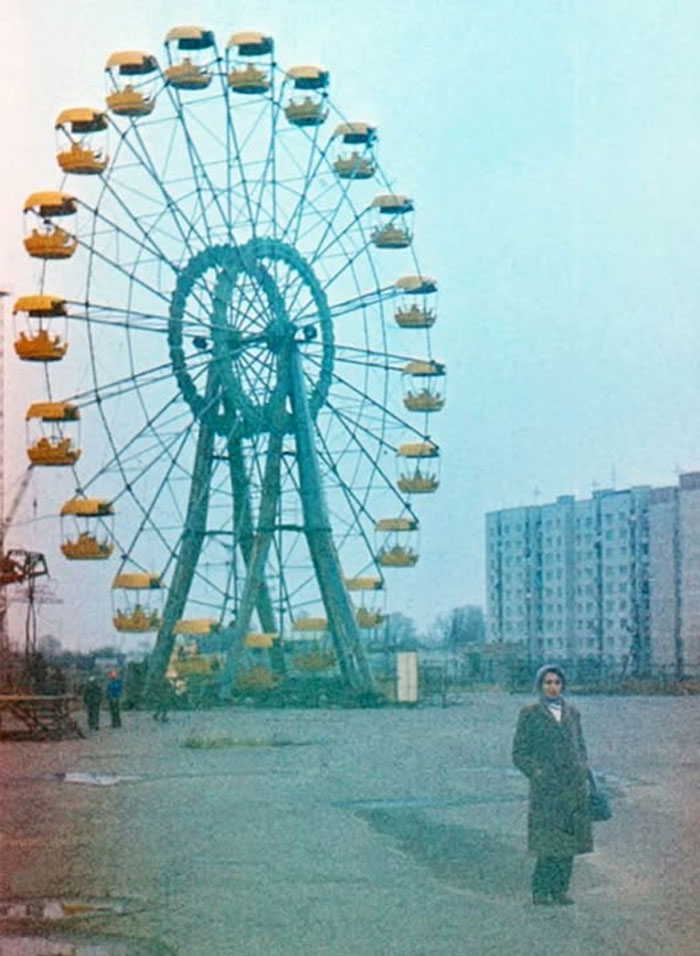 Vintage rare historical photo of a large Ferris wheel near apartment buildings with a woman standing in the foreground.