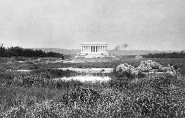 Rare historical photo showing Lincoln Memorial under construction with surrounding grassy fields and workers in early 1900s.