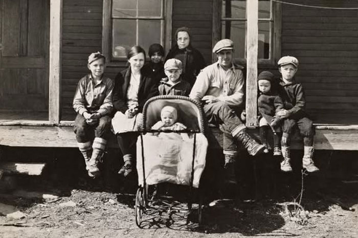 Rare historical photo of a family sitting on a wooden porch with a baby in a vintage stroller outdoors.