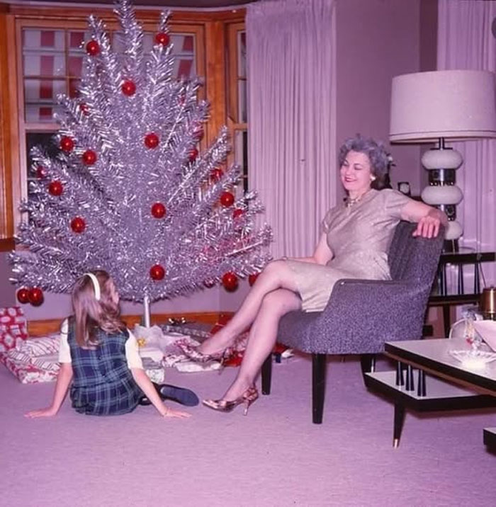 Vintage rare historical photo of a woman and child by a silver Christmas tree with red ornaments in a living room.