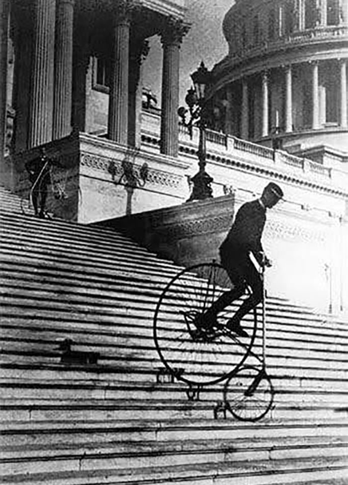 Man riding a vintage high-wheel bicycle down steep steps in a rare historical photo capturing a unique moment in time.
