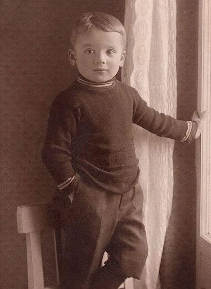 Vintage rare historical photo of a young boy standing by a window in early 20th century clothing.