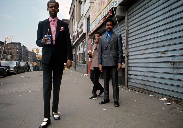 Three young men dressed in suits standing and walking on a city sidewalk in a rare historical photo.