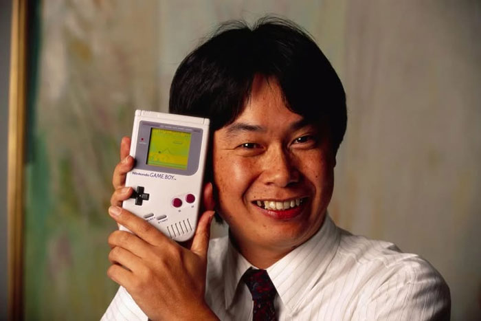 Inventor smiling and holding an original Nintendo Game Boy in rare historical photo capturing iconic technology moment