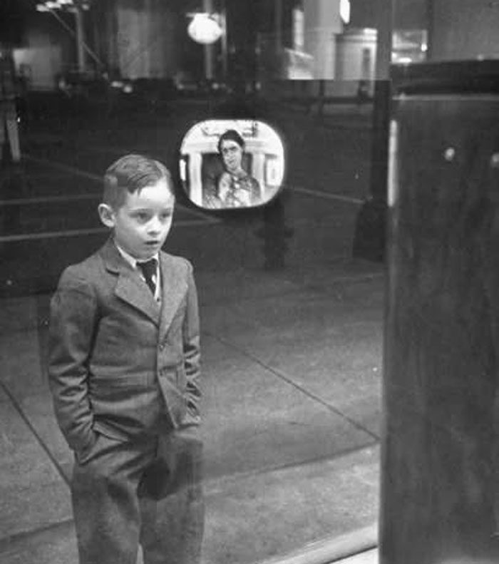 Young boy dressed in a suit watching an early television set in a rare historical photo capturing the world's past.