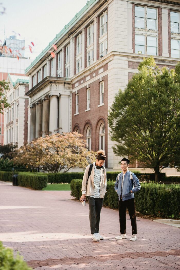 Two young men with backpacks standing outdoors near a college building, representing unethical life hacks in the real world.