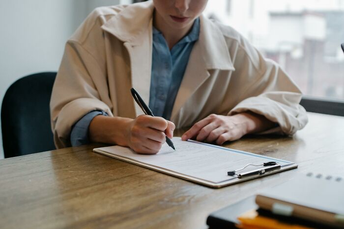 Person writing on paper with pen at wooden desk, illustrating unethical life hacks that helped win in the real world.