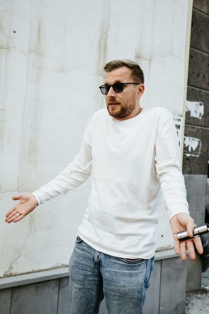 Man in sunglasses and white shirt shrugging with hands out, illustrating unethical life hacks to win in the real world.