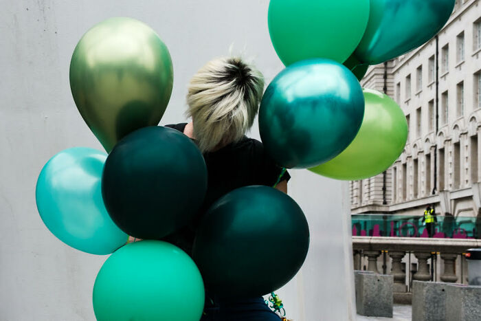 Person holding vibrant green and teal balloons in an urban setting, showcasing colorful candid street photos.