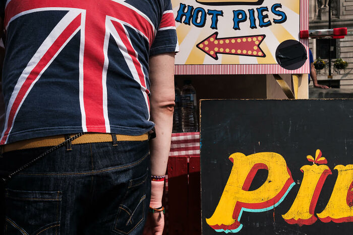 Man wearing a colorful shirt stands near vibrant street signs at a food stall in a candid street photo capturing life's moments.