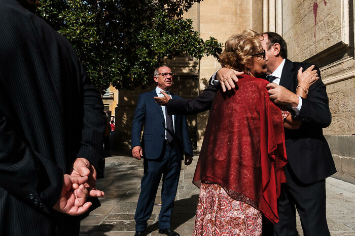 Candid street photo capturing colorful, emotional moments between people in an urban setting with strong sunlight and shadows.