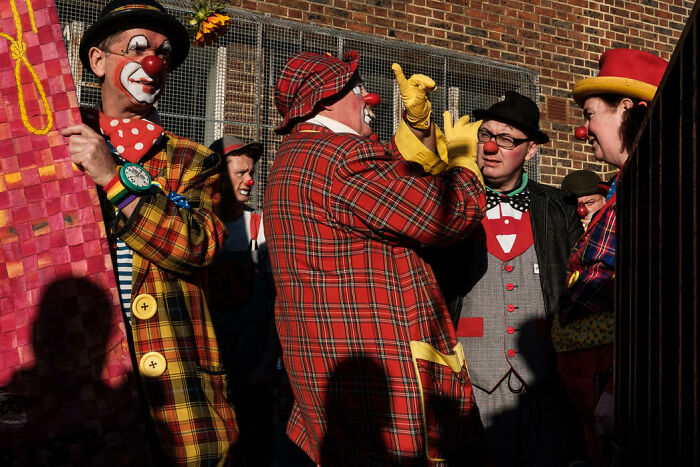 Clowns in colorful costumes share candid moments during a vibrant street scene capturing life’s colorful moments.