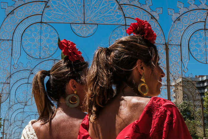 Two women with red flowers in their hair, wearing colorful clothing, captured in a vibrant candid street photo.