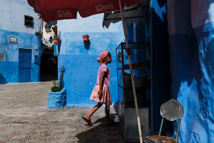 Young girl walking through vibrant blue street, showcasing colorful candid moments in stunning street photography.