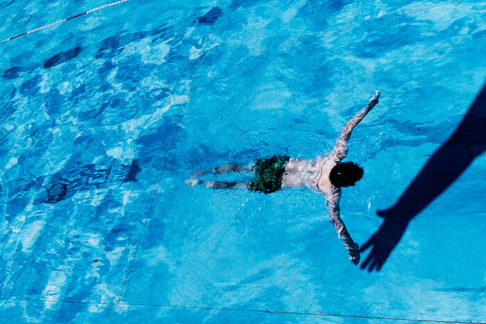 A colorful street photo capturing a candid moment of a person swimming in a bright blue pool.