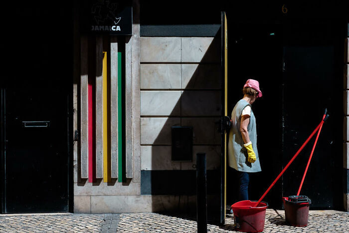 Woman with yellow gloves and pink hat mopping street in vibrant urban scene, showcasing stunning street photos candid moments.