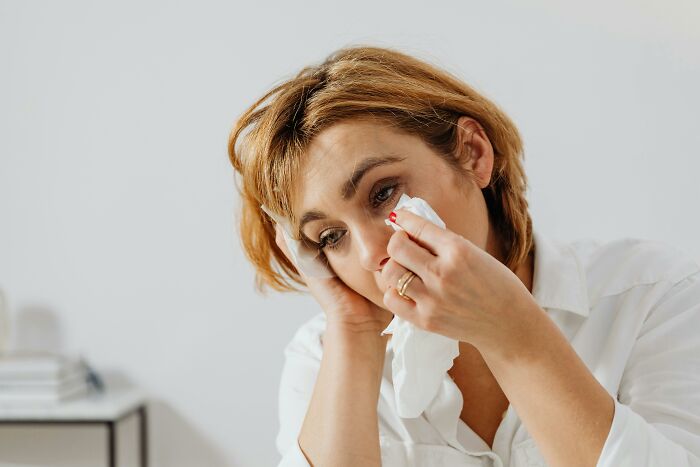 Woman wiping tears with a tissue in a bright room, illustrating emotions for an unpopular opinions poll discussion.