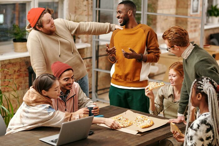 Group of diverse friends enjoying pizza and laughter while discussing an unpopular opinions poll in a casual workspace setting
