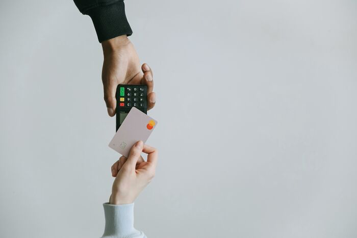 Hand holding a credit card near a payment terminal, illustrating concepts for unpopular opinions poll and transactions.