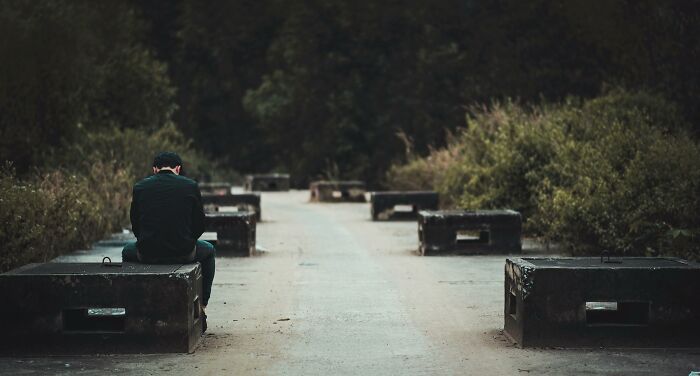 Person sitting alone on a concrete bench in a park, reflecting quietly in a scene fitting an unpopular opinions poll.