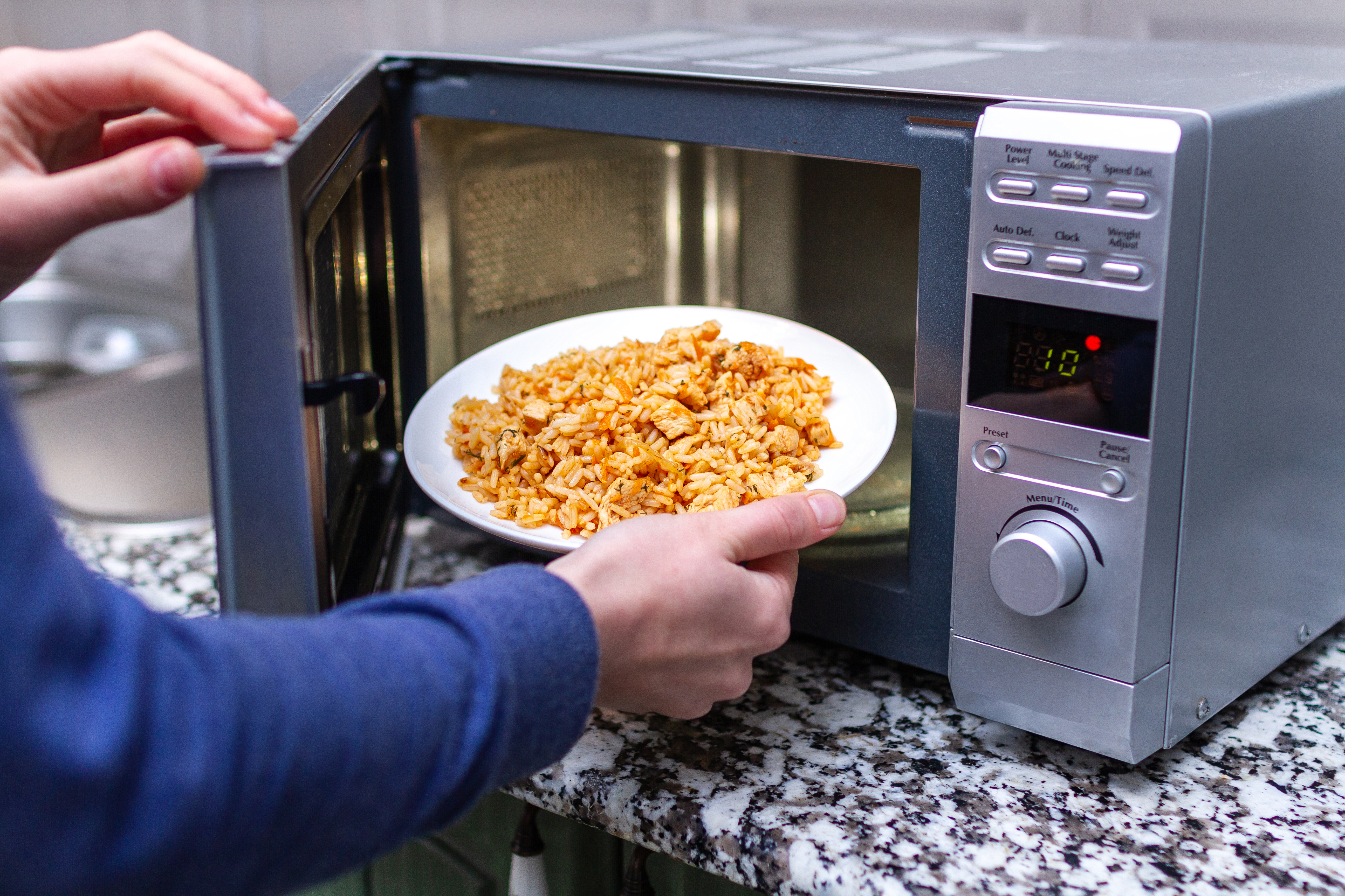 Person placing a plate of lunch into a microwave in an office kitchen setting, coworker lunch protein bars concept