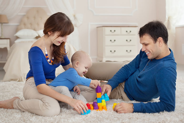 Young parents playing with their baby on the floor, illustrating vacation without kids babysitting and family time at home. Young parents playing with their baby on the floor, illustrating vacation without kids babysitting and family time at home.