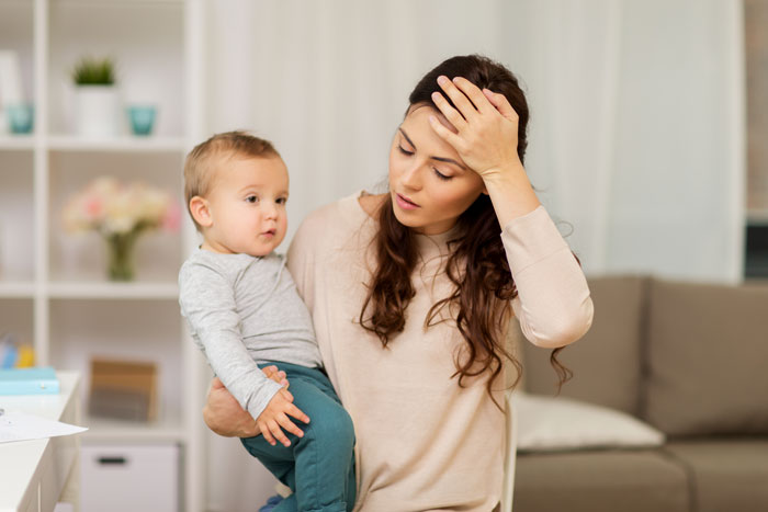 Tired mother holding young child indoors, illustrating the challenges of vacation without kids babysitting options. Tired mother holding young child indoors, illustrating the challenges of vacation without kids babysitting options.