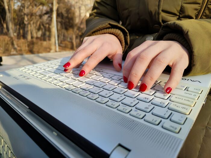 Hands with red nail polish typing on a laptop keyboard outdoors, illustrating a good trend slowly disappeared in technology use.