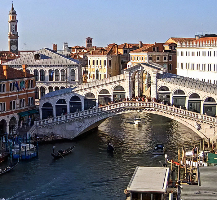 Rialto Bridge over Grand Canal in Venice with boats and historic buildings on a sunny day.