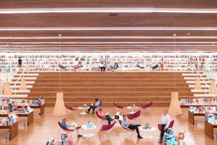 Spacious modern library with wooden decor and people reading, showcasing cosy and grandiose libraries from around the world.