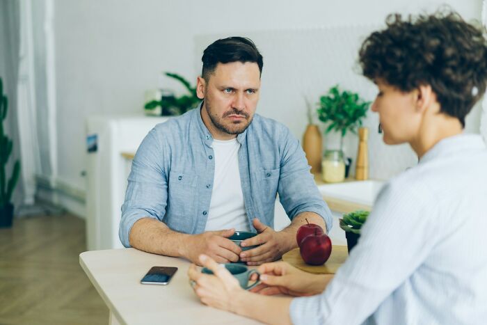 Man and woman having a serious conversation about pregnancy and twins while sitting at a kitchen table with apples nearby.