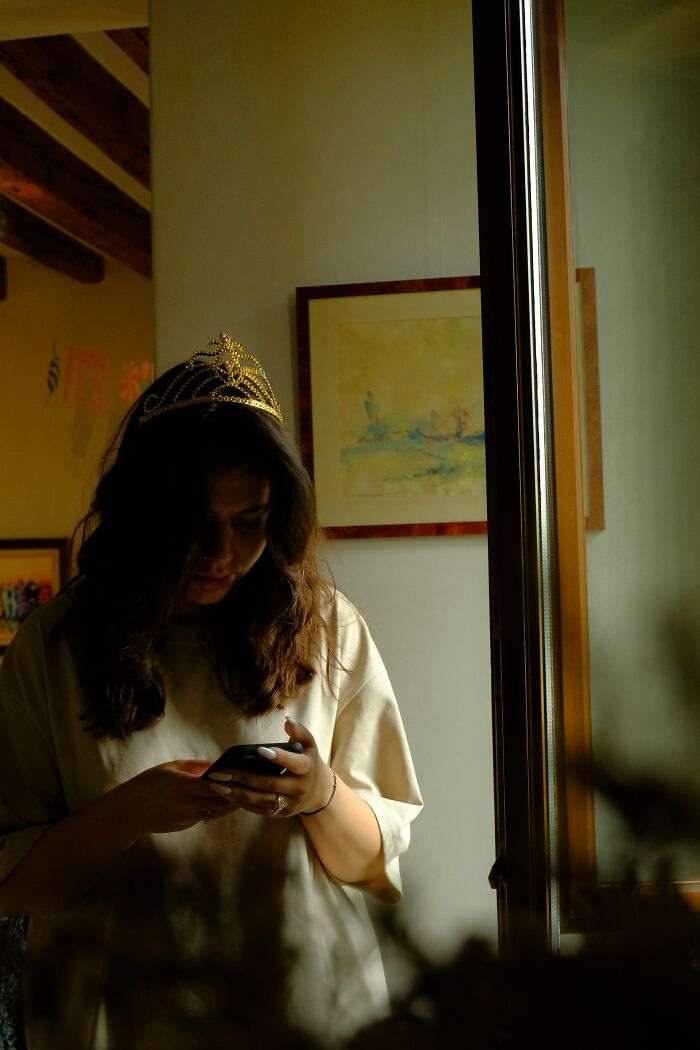 Young woman wearing a tiara looks down at her phone in a dimly lit room, reflecting moments people realized their friend was a jerk.