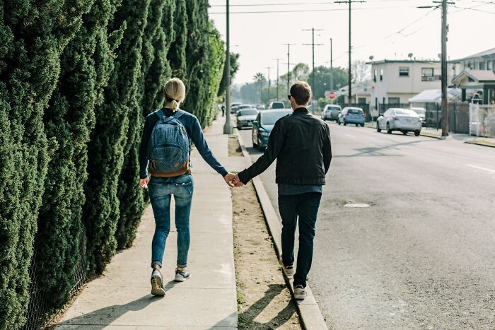 A couple walking hand in hand on a sidewalk beside tall greenery, illustrating behaviors that may indicate insecurity.