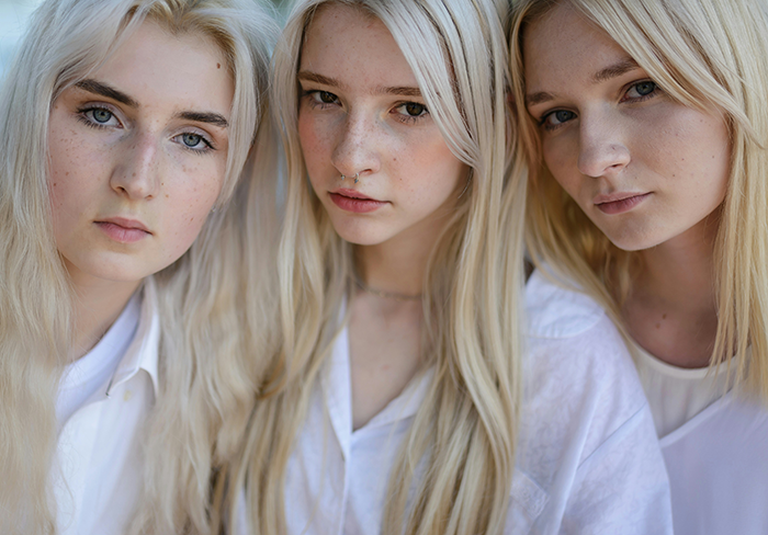 Three blonde triplets with serious expressions dressed in white, highlighting family favoring matching siblings over the other one.