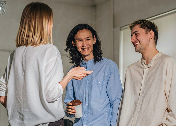 Three people having a friendly conversation indoors, illustrating social dynamics and microfeminism countering toxic masculinity.