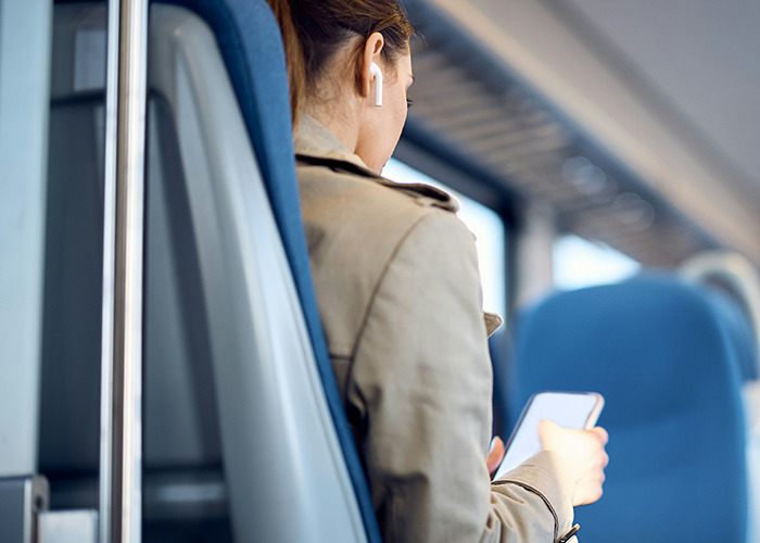 Woman wearing earbuds and holding smartphone on a train, illustrating microfeminism strategies against toxic masculinity.