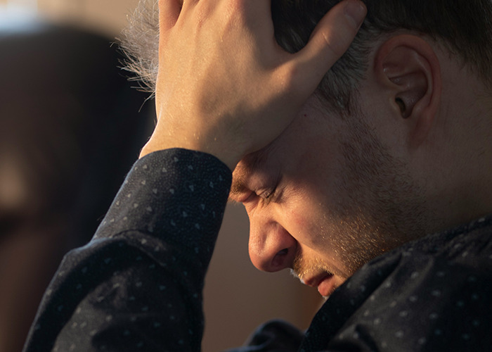 Man holding his head in frustration indoors, illustrating the impact of toxic masculinity on mental health.