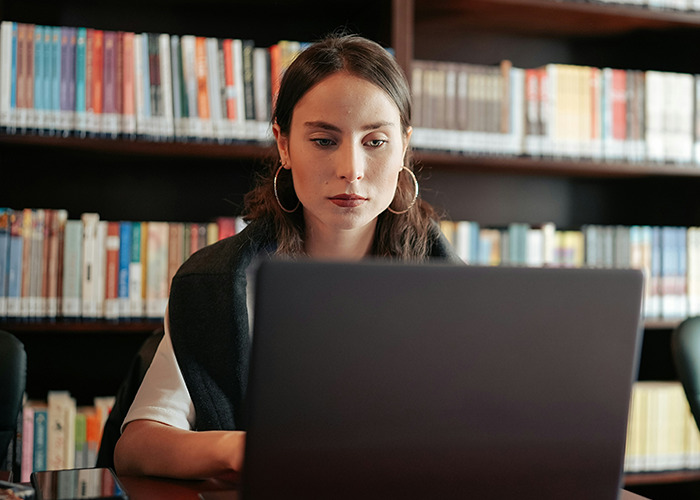 Woman focused on laptop in a library, representing microfeminism strategies countering toxic masculinity challenges.