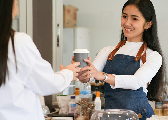 Young woman in an apron smiling and handing a coffee cup, illustrating microfeminism countering toxic masculinity in daily life.