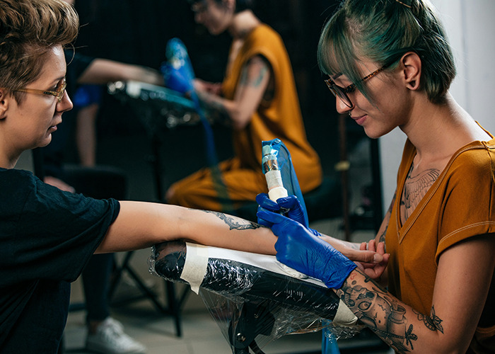 Tattoo artist with gloves creating detailed body art illustrating microfeminism empowering women against toxic masculinity.