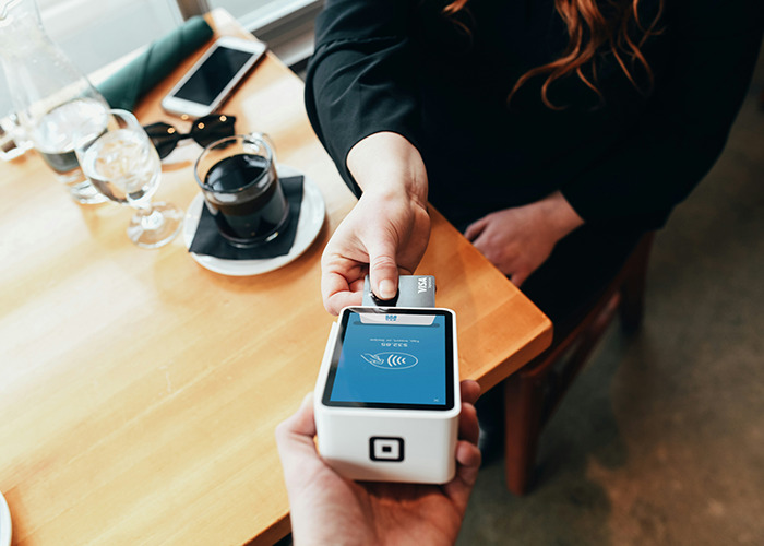 Woman using a contactless payment card with a mobile card reader, demonstrating microfeminism to counter toxic masculinity.