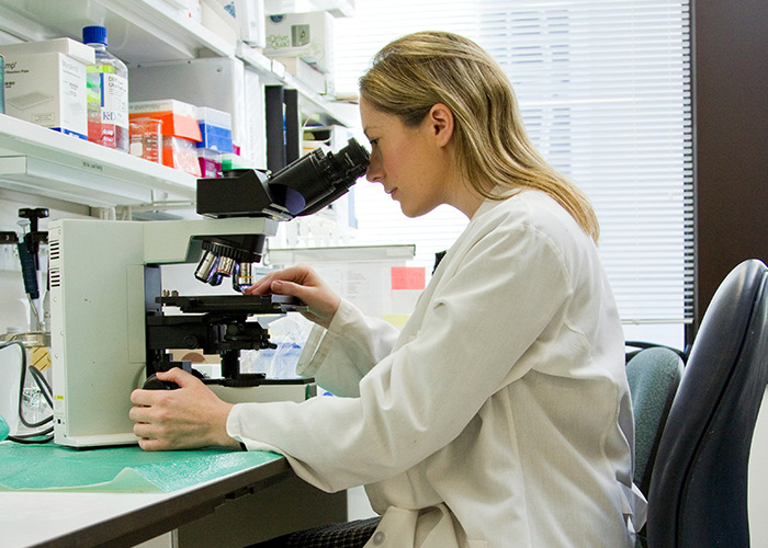 Woman in a lab coat using a microscope in a lab, symbolizing microfeminism challenging toxic masculinity.