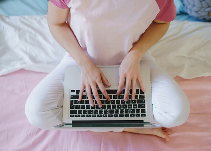 Woman wearing pink and white clothes typing on a laptop, illustrating microfeminism to counter toxic masculinity online.