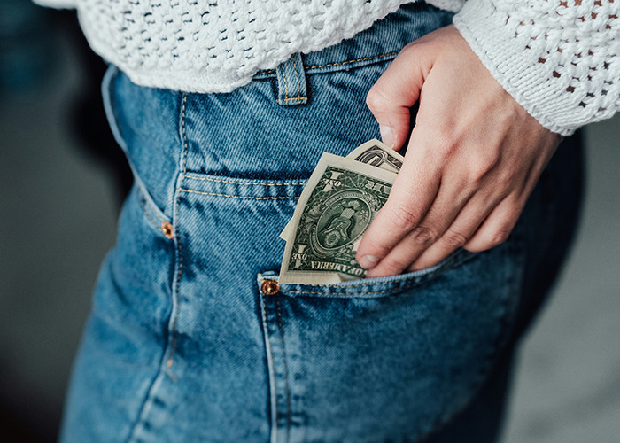 Woman wearing blue jeans and a white sweater placing cash in pocket, symbolizing microfeminism countering toxic masculinity.