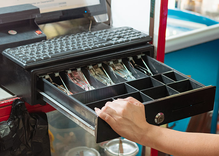 Hand opening cash register drawer at a checkout counter, security tape capturing a weird and random moment.
