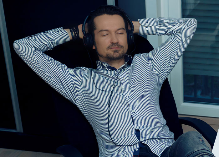 Man wearing headphones and striped shirt relaxing with eyes closed, capturing weird and random moments on security tape.