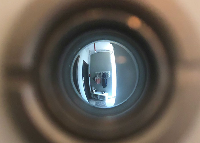 View through a peephole showing an interior hallway with a door and hanging clothes, capturing a weird security tape moment.