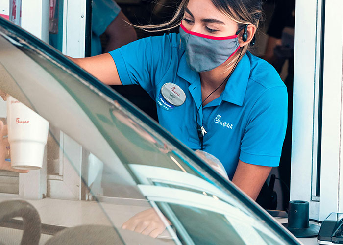 Fast food worker wearing a face mask and headset serving a customer at a drive-thru window caught on security tape