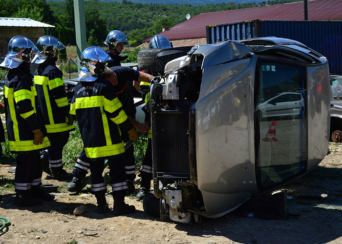 Firefighters in helmets inspecting a flipped car caught on security tape during a strange accident scene outdoors.