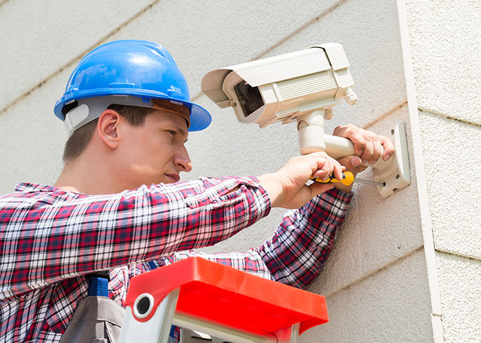 Technician in blue hard hat installing a security camera, capturing weird and scary moments on security tape footage.